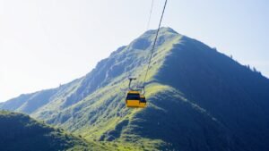 A bright yellow cable car ascends a green mountain.